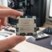 A human hand holds an AMD Ryzen 7 9700X processor close to the lens in a realistic home office.