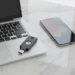 A black YubiKey 5C NFC hardware security key with a gold contact button sits on a wooden desk next to a laptop.