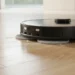 A black Dreame L50 Ultra robot vacuum and mop actively cleaning fine dust and debris off a light hardwood floor using its dual spinning mop pads.