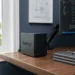 A compact black NAS unit sitting on a clean walnut desk in a home office, representing professional independent data storage solutions.